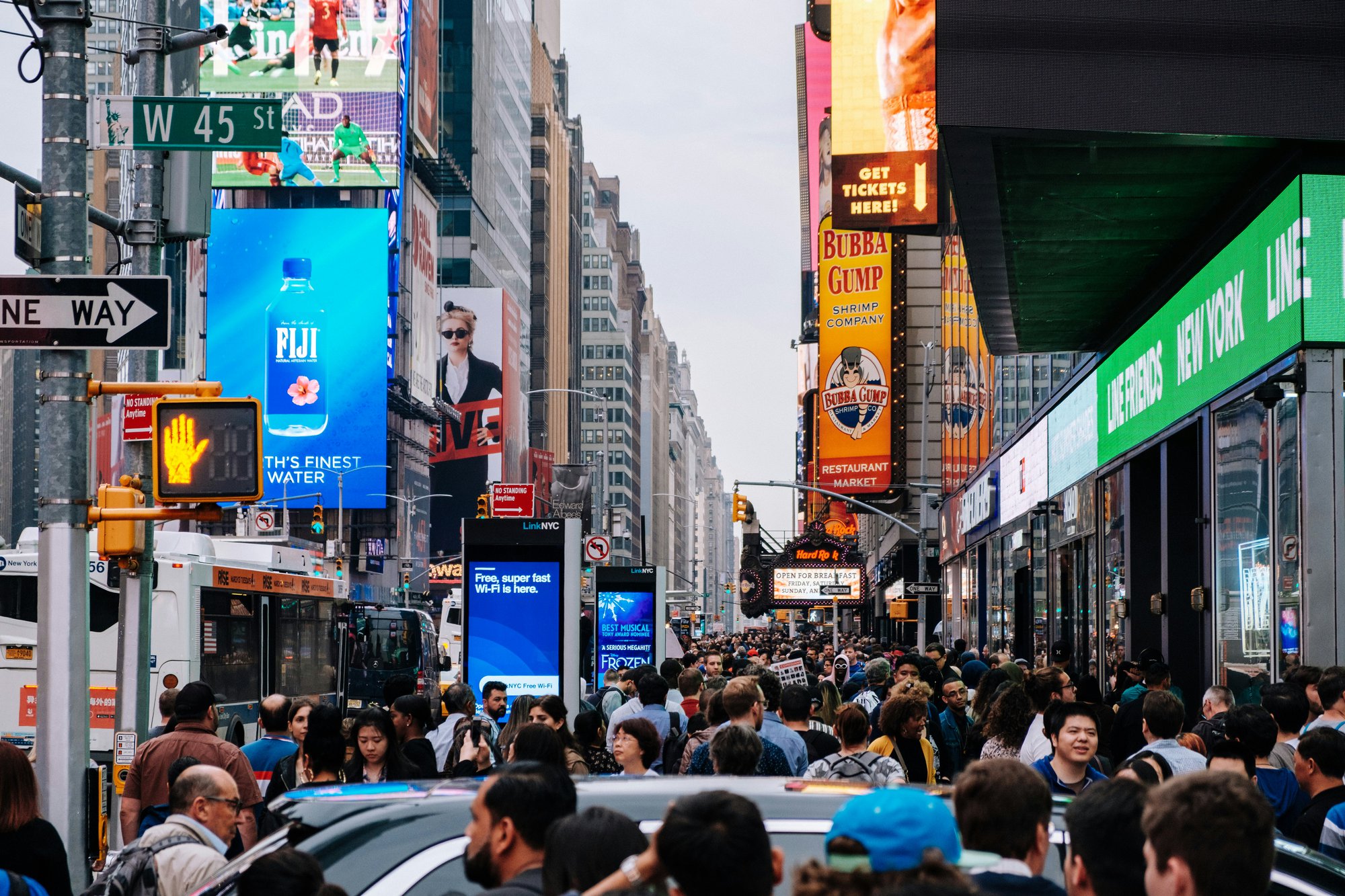 Busy street scene in New York City with crowds, traffic, and digital billboards
